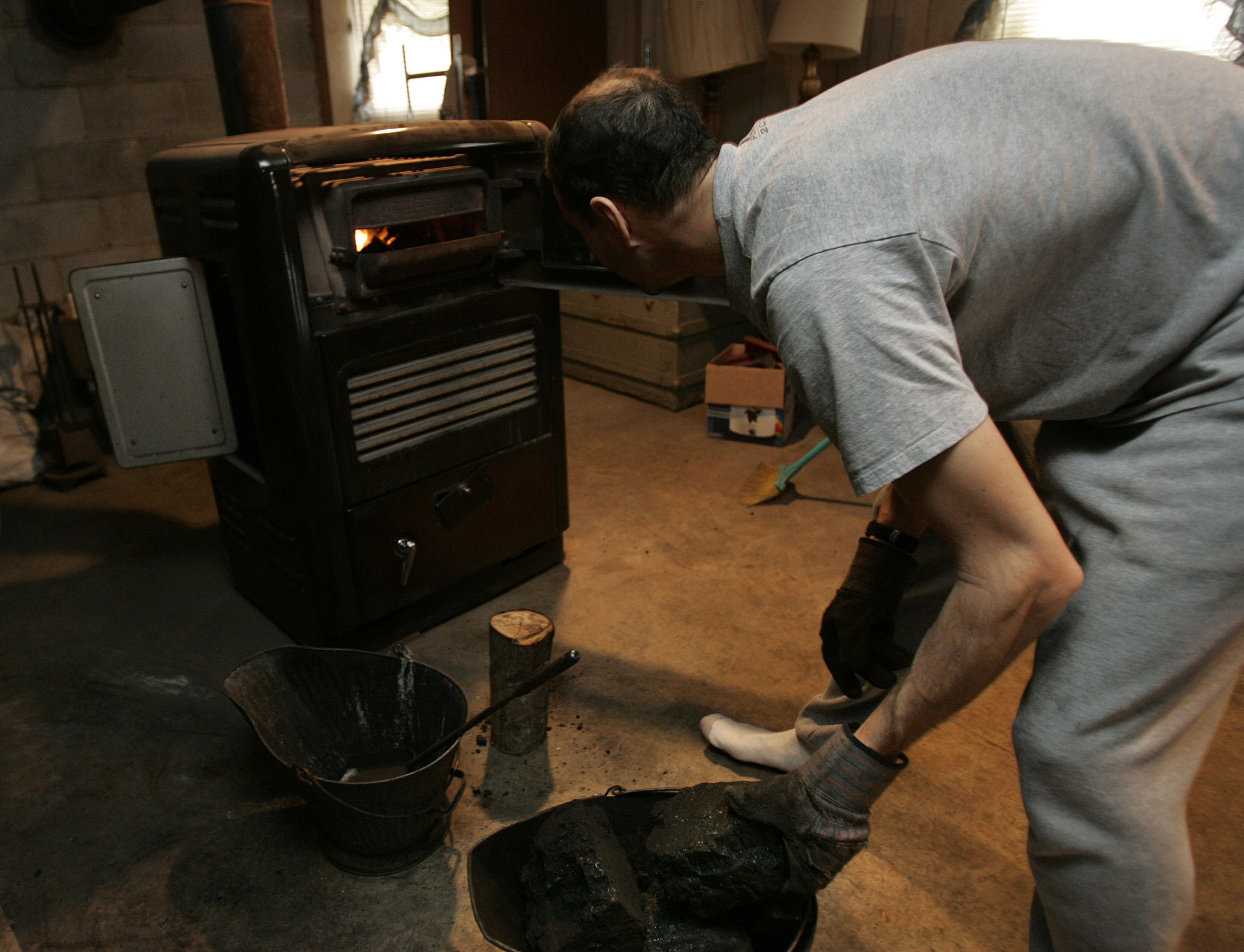 Мужчина топит угольную печь, которая обогревает дом
