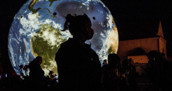 Женщина в маске стоит перед огромным надувным глобусом в Праге