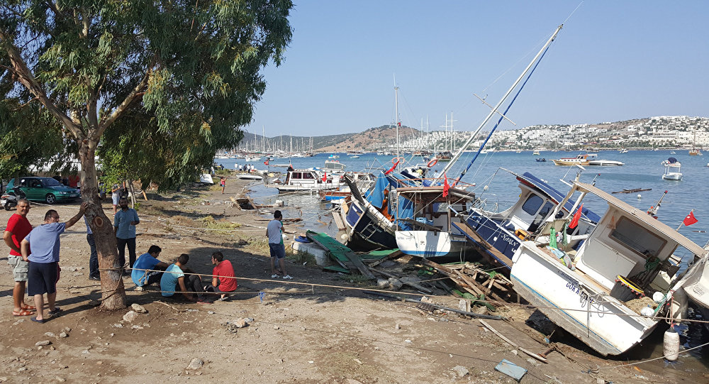 Люди стоят рядом с поврежденными лодками, после мощного землетрясения в Эгейском море у побережья Турции