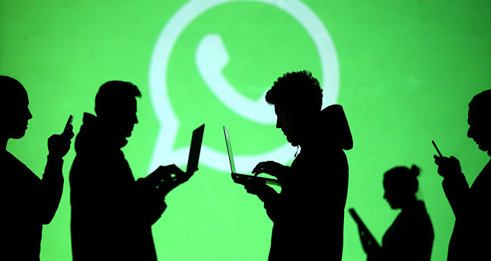 Силуэты людей на фоне логотипа мессенджера WhatsApp. Архивное фото