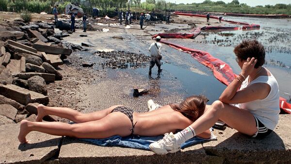 Отдыхающие рядом с рабочими во время очистки пляжа от нефти в Аргентине, 1999 год  - Sputnik Кыргызстан
