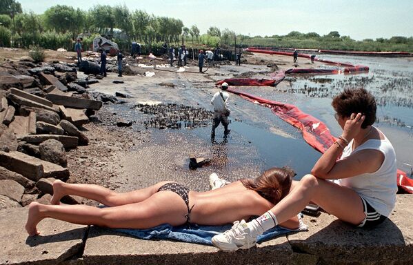 Отдыхающие рядом с рабочими во время очистки пляжа от нефти в Аргентине, 1999 год  - Sputnik Кыргызстан