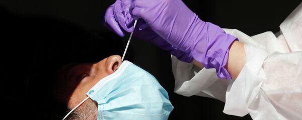 Медицинский работник в защитном костюме и лицевой маске берет мазок для ПЦР-теста на COVID-19 - Sputnik Кыргызстан