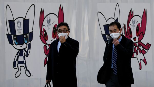 Мужчины в защитных масках на фоне талисмана Олимпийских игр 2020 в Токио (Япония)  - Sputnik Кыргызстан