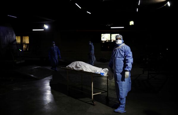 Медицинский работник в средствах индивидуальной защиты рядом с телом мужчины, умершего от COVID-19, перед кремацией в крематории в Нью-Дели, Индия - Sputnik Кыргызстан