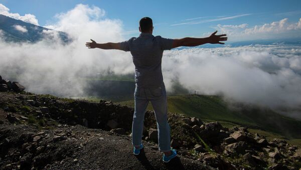 Мужчина раскинув руки стоит на фоне верблюжего перевала Тоо-Ашуу окутанного облаками - Sputnik Кыргызстан