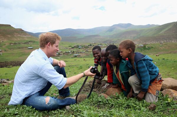 Британский принц Гарри показывает детям фотографию, которую он сделал на камеру во время посещения вечерней школы для мальчиков в Лесото - Sputnik Кыргызстан
