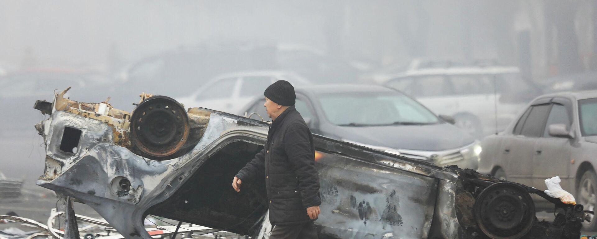 Мужчина проходит мимо машины, сгоревшей во время акций протеста в Алматы - Sputnik Кыргызстан, 1920, 06.01.2022