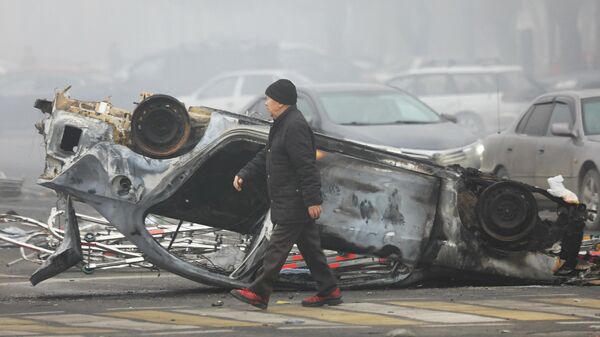 Мужчина проходит мимо машины, сгоревшей во время акций протеста в Алматы - Sputnik Кыргызстан