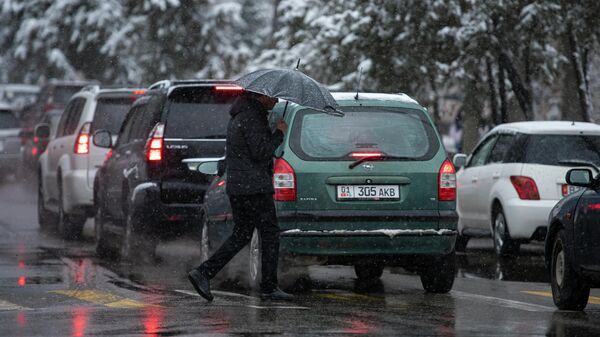 Мужчина с зонтом переходит дорогу во время снегопада в Бишкеке - Sputnik Кыргызстан