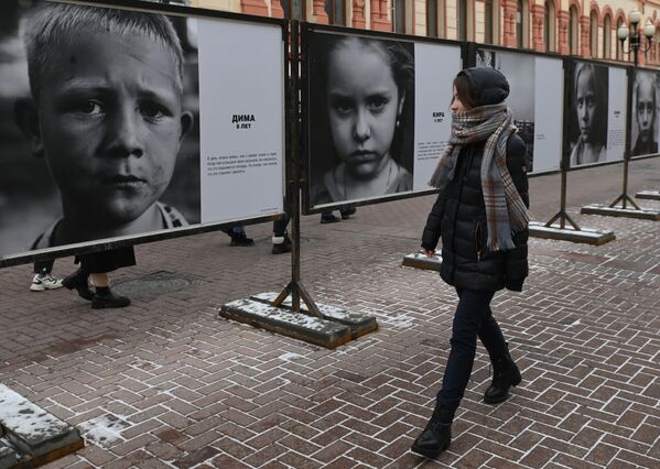 Девушка на Арбате в Москве смотрит на фотовыставку &quot;Посмотри в глаза Донбассу&quot;, на которой представлены фотографии детей из зоны боевых действий в Донбассе - Sputnik Кыргызстан