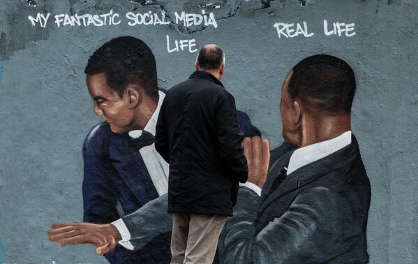 Мужчина смотрит на фреску берлинского уличного художника Эме Вольнодумца с изображением американского актера Уилла Смита, который дает пощечину комику Крису Року на церемонии вручения премии &quot;Оскар&quot; - Sputnik Кыргызстан