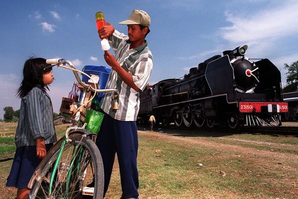 Камбоджиец набирает мороженое для маленькой девочки. За ними старый паровоз &quot;Пасифик 231&quot; останавливается на небольшой станции в 50 километрах к югу от Пномпеня. 2000 - Sputnik Кыргызстан