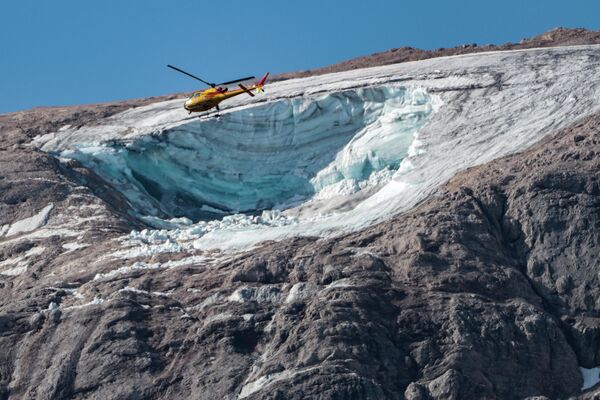 Спасательный вертолет пролетает над ледником, рухнувшим на самой высокой в Доломитовых Альпах горе Мармолада. До этого на вершине зафиксировали рекордно высокую температуру в +10 градусов по Цельсию. Спасатели возобновили поиск выживших после схода лавины, в результате которого погибли по меньшей мере шесть человек и восемь получили травмы. - Sputnik Кыргызстан