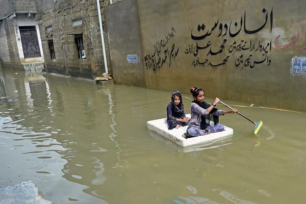 Девочки переплывают на временном плоту затопленную улицу в жилом районе после проливных муссонных дождей в Карачи. 26 июля. Из-за ливней в Карачи объявлено чрезвычайное положение. - Sputnik Кыргызстан