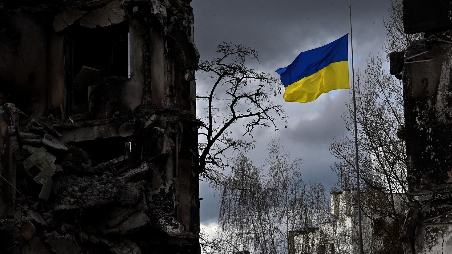 Украинский флаг между разрушенными во время бомбардировки зданиями в Киевской области. Архивное фото - Sputnik Кыргызстан, 1920, 25.11.2022