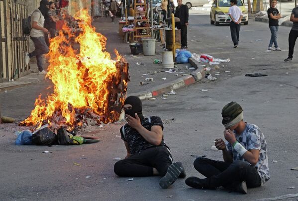 Палестинские демонстранты сидят возле горящих шин на фоне столкновений с израильскими силами безопасности в городе Хевроне на оккупированном Западном берегу - Sputnik Кыргызстан