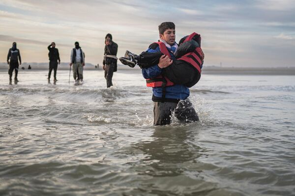 Беженец несет ребенка на пляже Гравелин, пытаясь пересечь пролив Ла-Манш (Франция) - Sputnik Кыргызстан