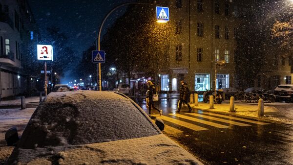 Припаркованная машина покрыта снегом, когда люди идут по пешеходному переходу во время раннего снегопада в Берлине. Архивное фото - Sputnik Кыргызстан