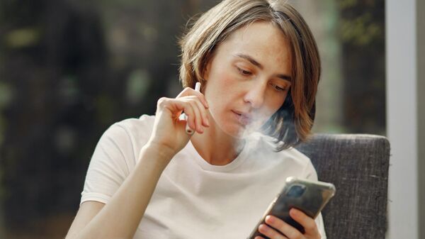 Девушка смотрит на телефон во время курения электронных сигарет. Иллюстративное фото - Sputnik Кыргызстан