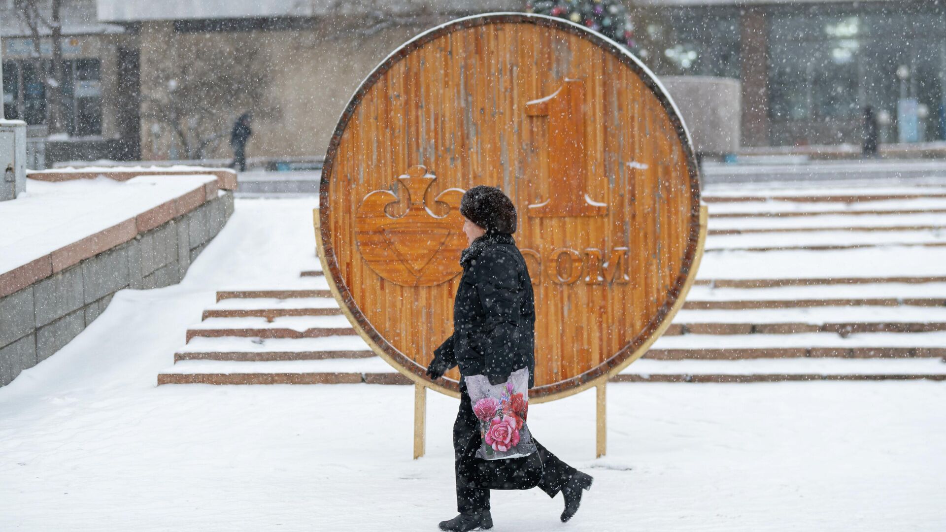 Женщина проходит возле деревянной инсталляции 1 сому во время снегопада в Бишкеке. Архивное фото - Sputnik Кыргызстан, 1920, 16.01.2023