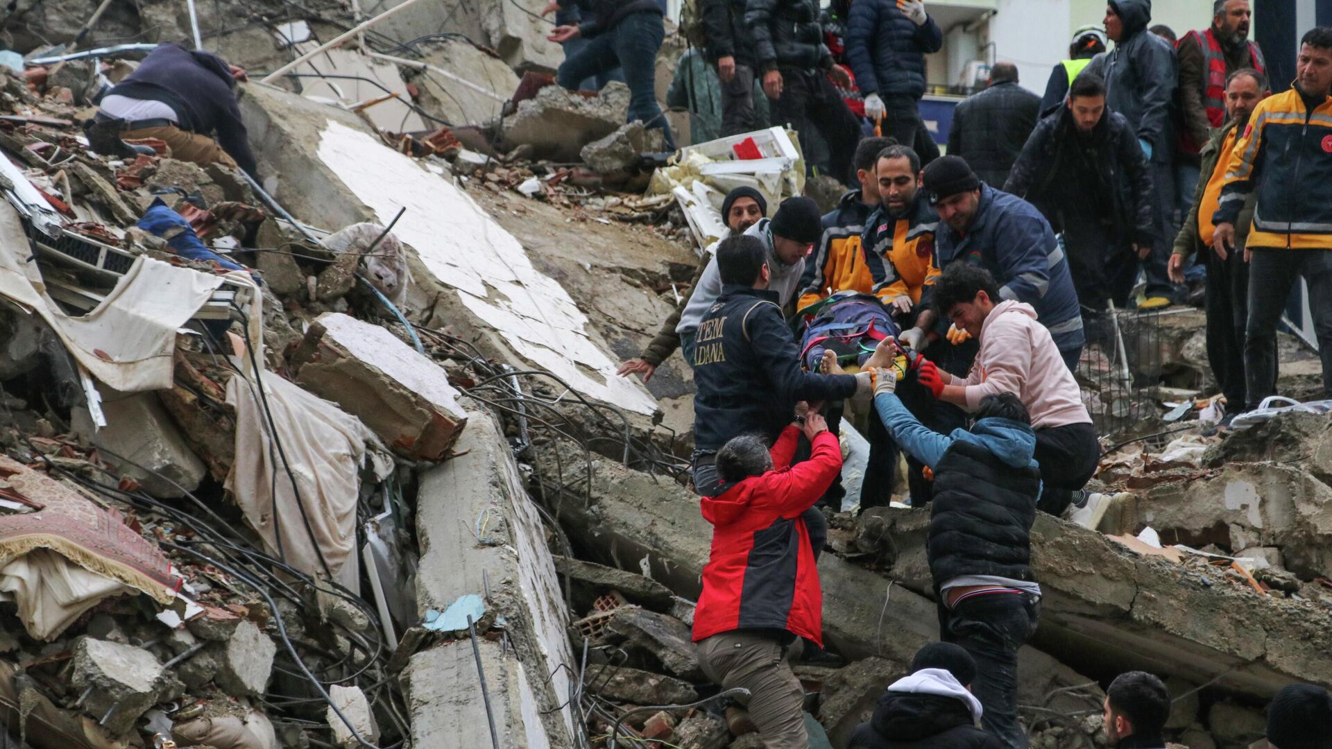 Люди и спасатели выносят пострадавшего из рухнувшего здания в Адане, Турция - Sputnik Кыргызстан, 1920, 06.02.2023