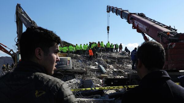 Люди смотрят на спасателей, ищущих выживших среди разрушенных зданий в Нурдагы - Sputnik Кыргызстан