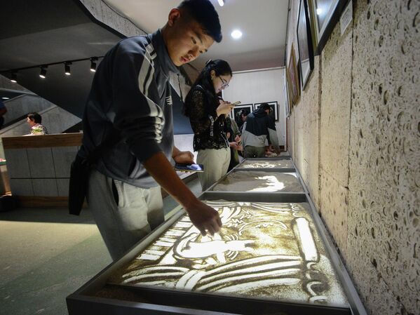 Посетитель музея пытается нарисовать картину песком   - Sputnik Кыргызстан