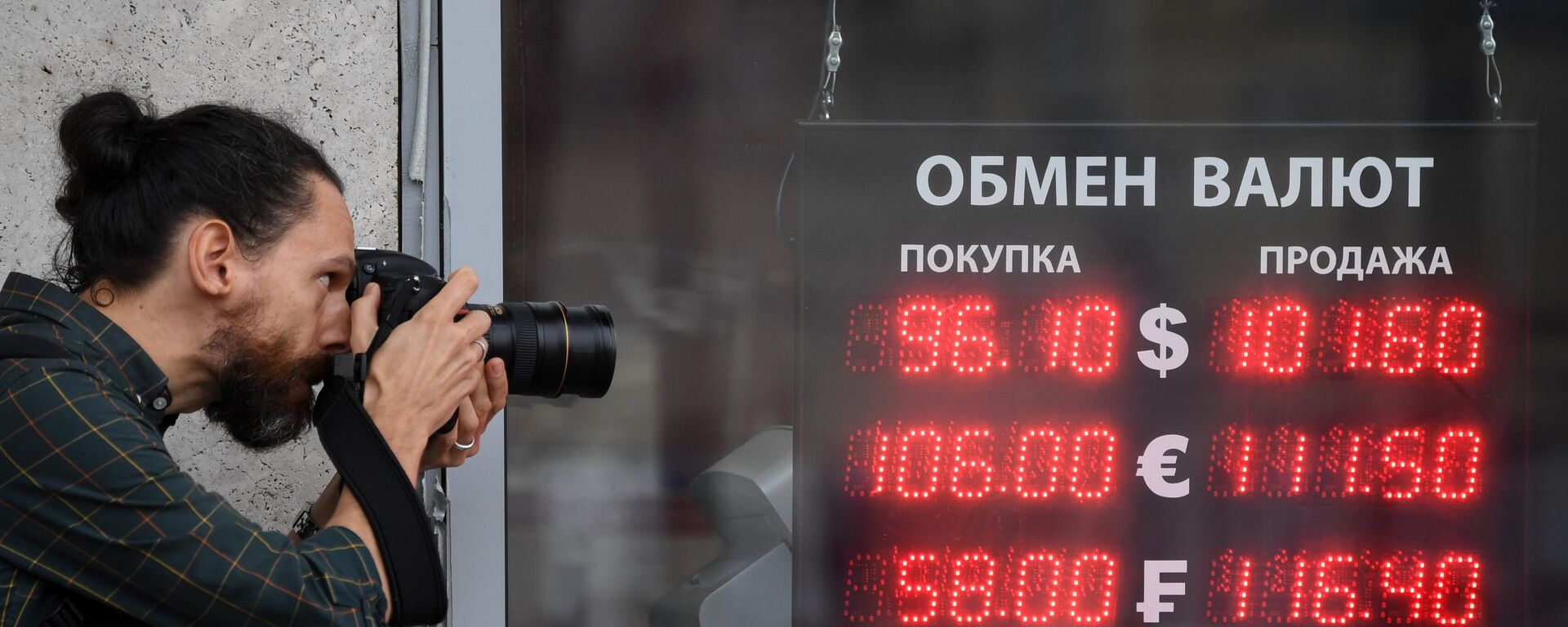 Мужчина фотографирует электронное табло у пункта обмена валют в Москве - Sputnik Кыргызстан, 1920, 29.08.2023