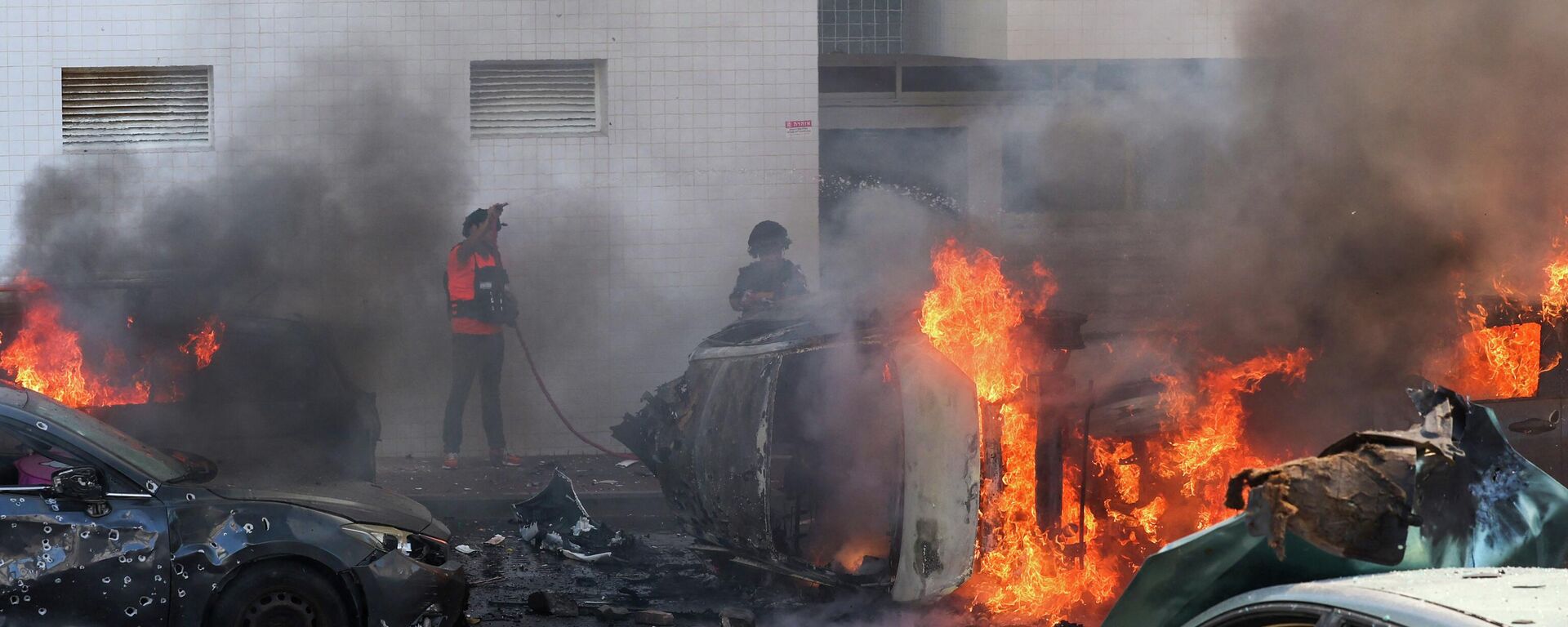Люди пытаются тушить пожар в автомобилях после ракетного обстрела из сектора Газа в Ашкелоне, на юге Израиля - Sputnik Кыргызстан, 1920, 07.10.2023