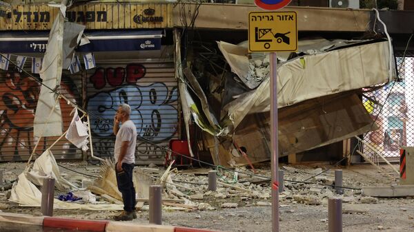 Мужчина стоит перед поврежденным магазином в Тель-Авиве после того, как в него попала ракета, выпущенная палестинскими боевиками из сектора Газа - Sputnik Кыргызстан