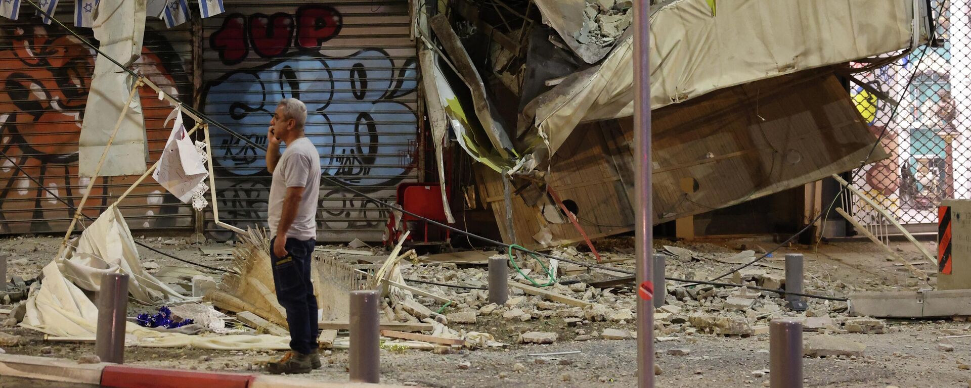 Мужчина стоит перед поврежденным магазином в Тель-Авиве после того, как в него попала ракета, выпущенная палестинскими боевиками из сектора Газа - Sputnik Кыргызстан, 1920, 10.10.2023