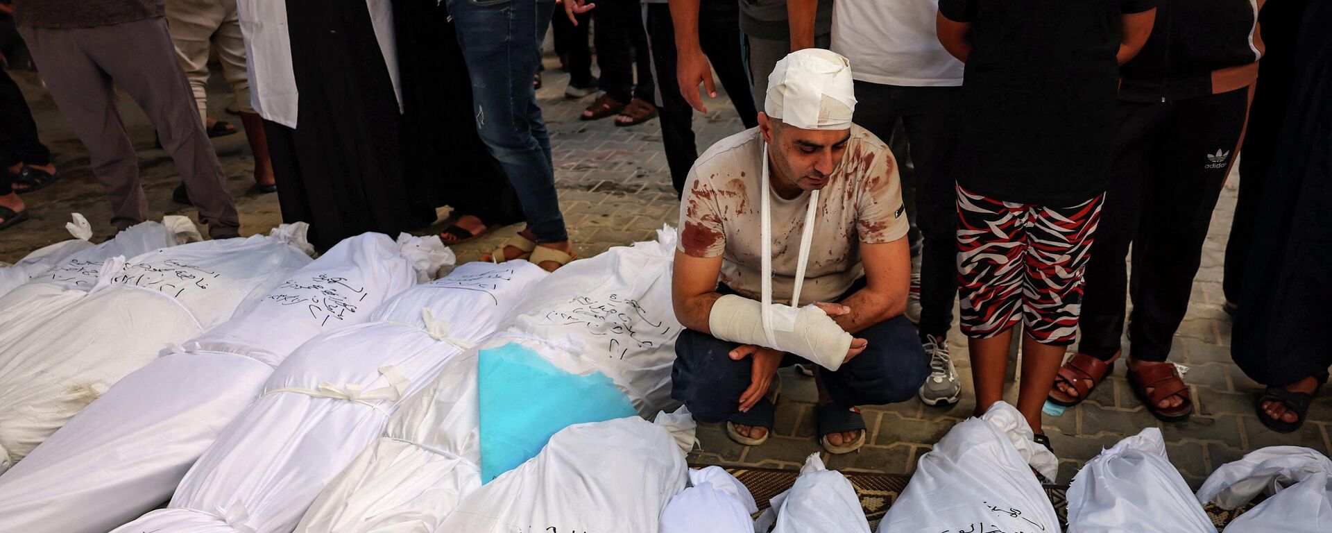 Раненый палестинец возле трупов своих детей, лежащих среди других тел, погибших в результате израильской бомбардировки на юге сектора Газа - Sputnik Кыргызстан, 1920, 25.10.2023