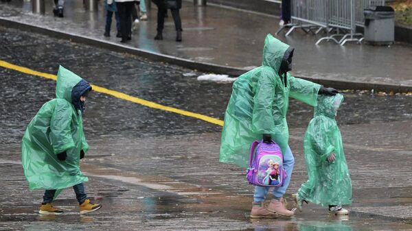 Женщина с детьми идут по дороге в дождевиках в дождливую погоду - Sputnik Кыргызстан