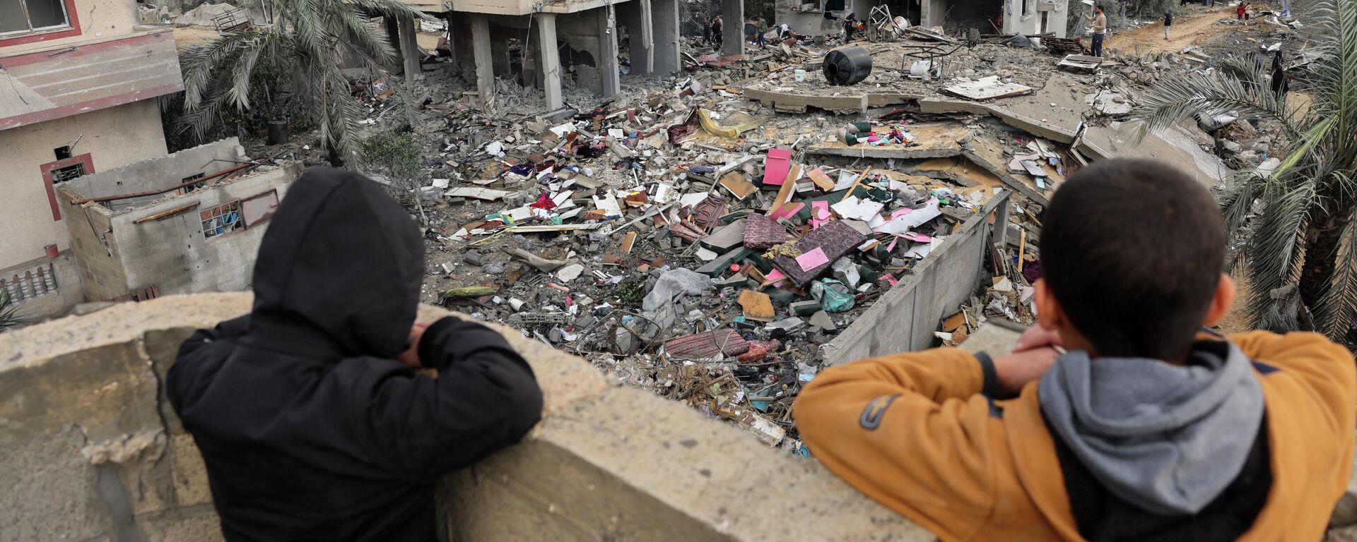 Палестинские дети смотрят, как люди стоят на обломках здания, разрушенного во время израильских ударов по Рафаху на юге сектора Газа. - Sputnik Кыргызстан, 1920, 02.12.2023