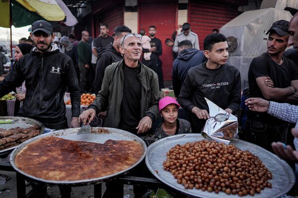 В этот день люди ходят в гости, дарят подарки и накрывают столы. На фото: продавцы продают сладкую выпечку на рынке в Дейр-эль-Балахе в центре сектора Газа.  - Sputnik Кыргызстан