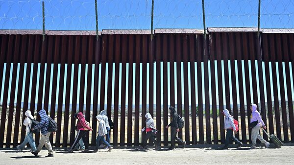 Мигранты идут по американской стороне пограничной стены в Джакумба-Хот-Спрингс, после перехода из Мексики - Sputnik Кыргызстан