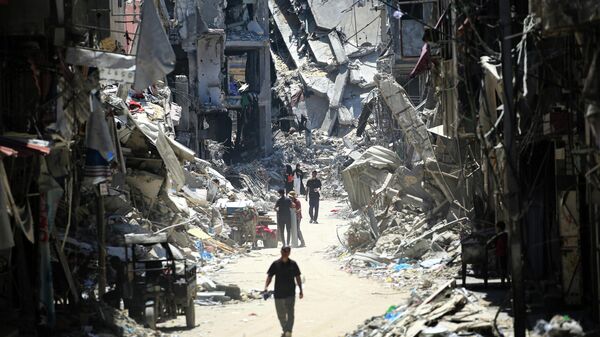 Палестинцы идут по узкой улице мимо разрушенных зданий в Хан-Юнисе на юге сектора Газа - Sputnik Кыргызстан