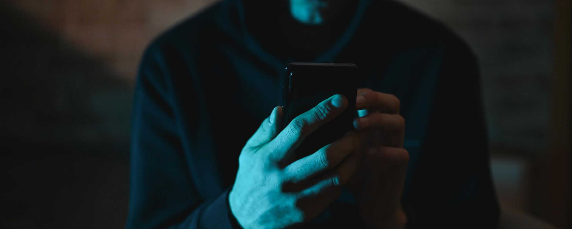 Мужчина в капюшоне со смартфоном в руках. Иллюстративное фото - Sputnik Кыргызстан, 1920, 17.10.2025