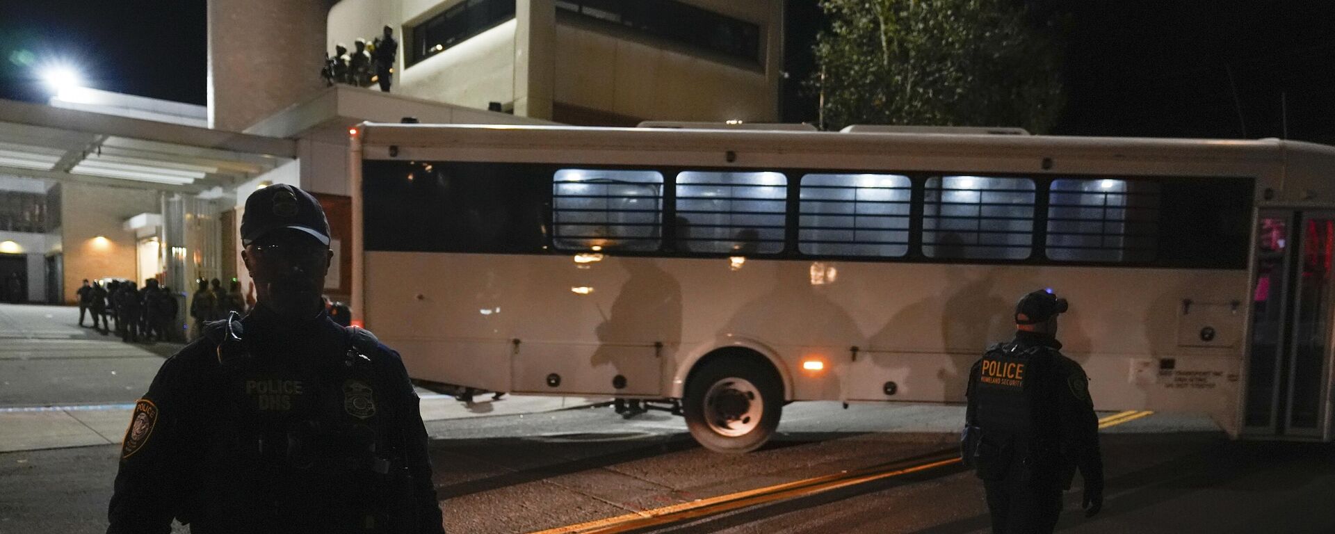 Портлендде АКШнын Иммиграция жана бажы кызматы (ICE) имаратынын сыртында турушкан укук коргоо органдарынын кызматкерлери автобустун жөнөшүн күтүп жаткан учурда - Sputnik Кыргызстан, 1920, 29.10.2025