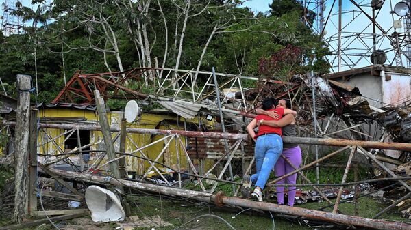 Электр линиясынын оператору Карлос Брачонун эжеси Эрика Утера АКШнын аба соккусунан телефон жана телевизор мунарасын талкалап, анын үйүнүн үстүнө кулап, кошунасын өлтүрүп, кызын жарадар кылган урандылардын жанында үй-бүлө мүчөсүн кучактап жатат. Каракастын чет жакаларында, Венесуэла. - Sputnik Кыргызстан