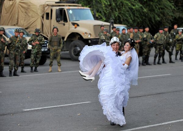 Только что поженившаяся пара позирует для фотографа на фоне полицейских в Оше 9 октября 2010 года. - Sputnik Кыргызстан