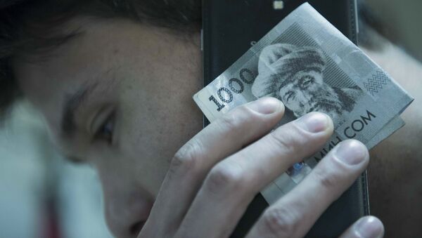 Мужчина держит сомовую валюту с мобильным телефоном. Архивное фото - Sputnik Кыргызстан