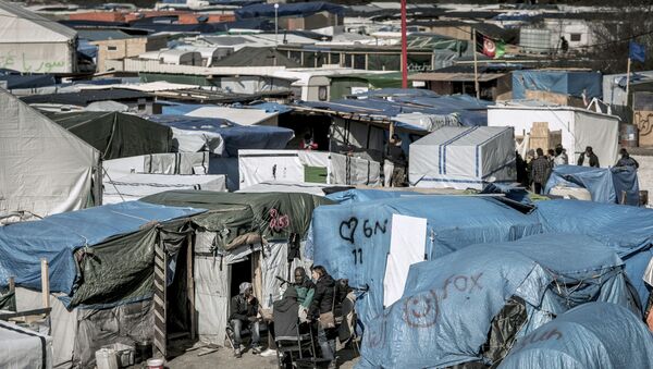 Мигранты за пределами палаток в самом большом нелегальном лагере вдоль северного побережья Франции, в портовом городе Кале. Архивное фото - Sputnik Кыргызстан