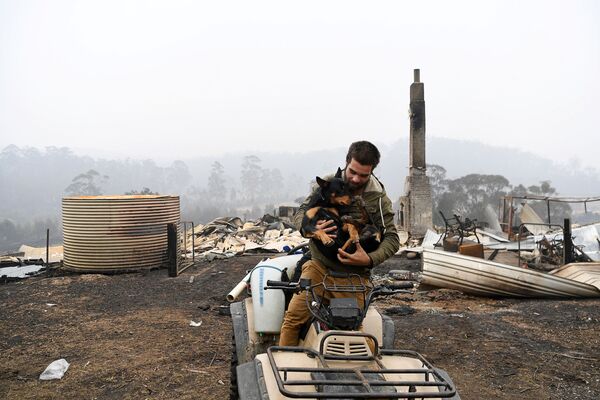 Мужчина с собакой на фоне сгоревшего дома в Австралии - Sputnik Кыргызстан
