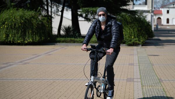 Молодой человек в защитной маске на велосипеде в городе - Sputnik Кыргызстан