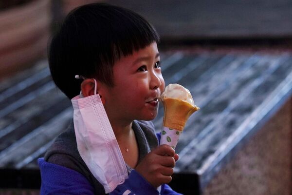 Ребенок с медицинской маской ест мороженое в первый день открытия магазина в Сяньнин, Китай - Sputnik Кыргызстан