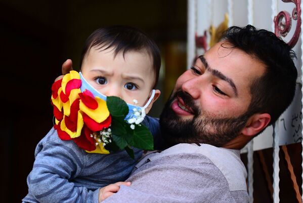 Мужчина с ребенком в украшенной цветами защитной маске в Эн-Наджафе, Ирак - Sputnik Кыргызстан