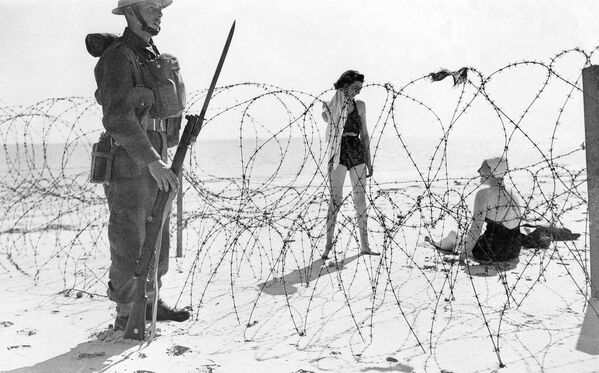 Девушки на пляже и солдат у колючей проволоки на пляже в Англии, 21 сентября 1940 года - Sputnik Кыргызстан